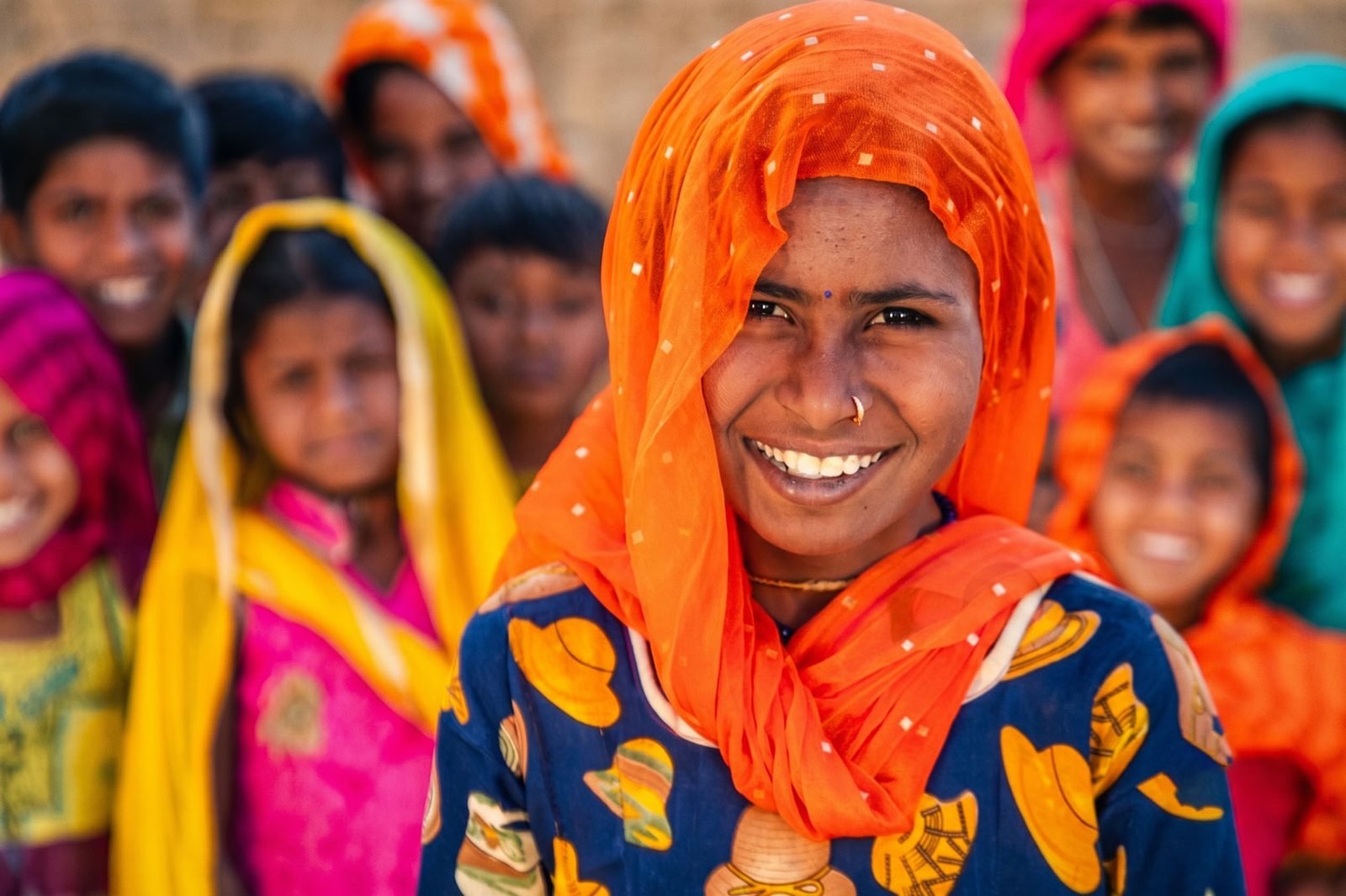A young woman smiling directly at the camera, surrounded by women and girls from her community
